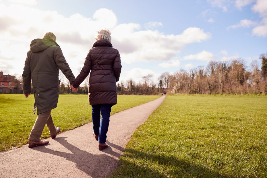 two seniors in coats holding hands as they go for a walk outside